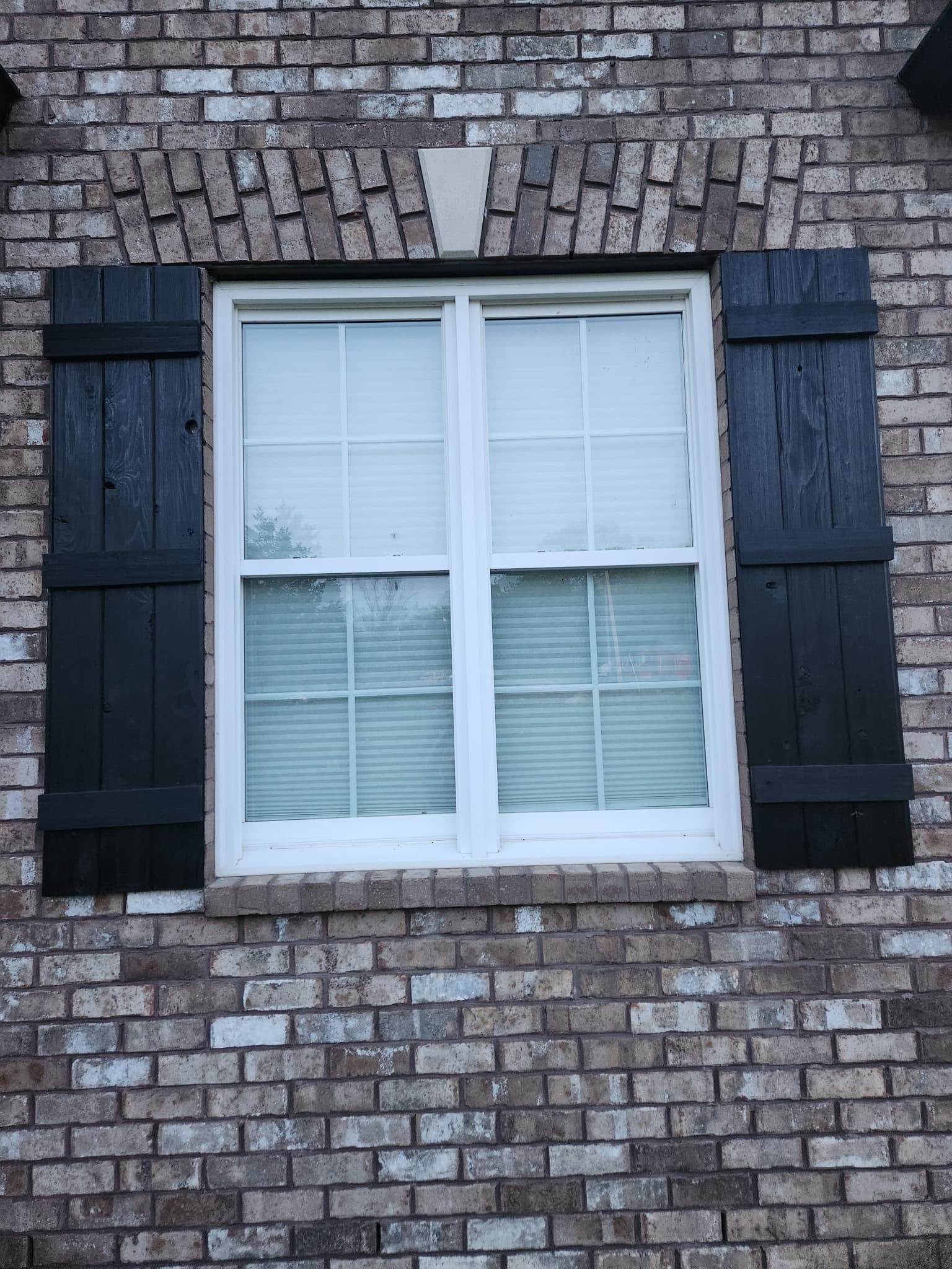 Wide shot: black 3-batten cedar shutters on a brick home